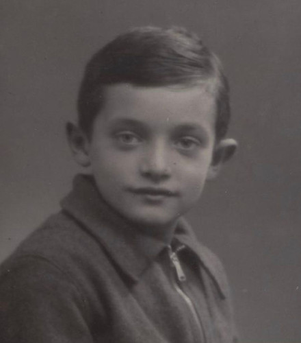 Black and white portrait of a young boy wearing a collared shirt and sweater, looking slightly to his right with a subtle expression.