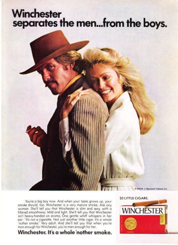 1973 print cigarette ad stating:

"Winchester separates the men...from the boys.

You're a big boy now. And when your taste grows up, your smoke should, too. Winchester is a very mature smoke. Ask any woman. She'll tell you that Winchester is slim and sexy, with a filtered smoothness. Mild and light. She'll tell you that Winchester isn't heavy-handed on aroma. One gentle whiff whispers in her ear: "It's not a cigarette. Not just another little cigar. It's a whole 'nother smoke. Very adult. And she'll tell you that when you're man enough for Winchester, you're man enough for her.

Winchester. It's a whole 'nother smoke."

It shows a pale long haired blonde wearing white with a huge smile hugging the back of a tanned short haired blonde with a mustache wearing a cowboy hat and a corduroy jacket with said cigarette in their hand.