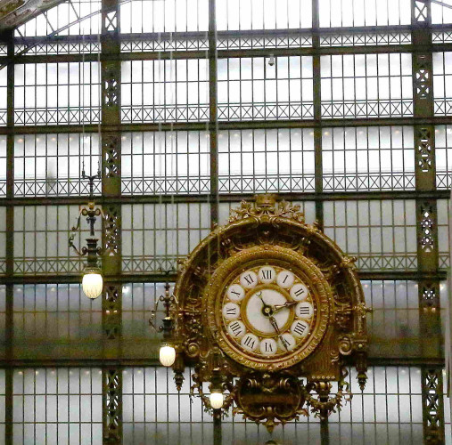 A very large window with walkways behind and a large, ornate clock in front.