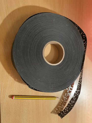 A punched tape with a pencil for scale.