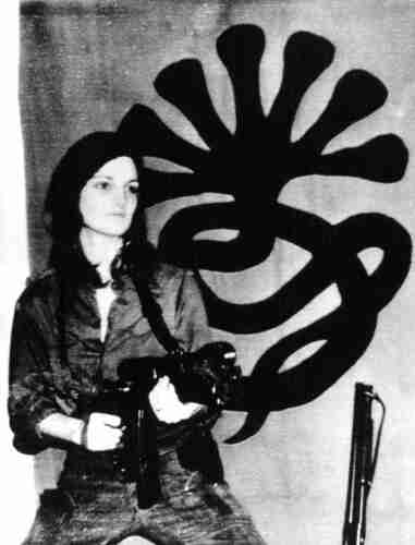 Patty Hearst posing with a machine gun in front of the Symbionese Liberation Army flag
