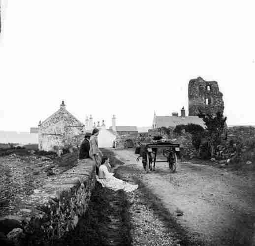 Original caption from source: Road approaching village, ruin to right, side-car, tourist party, a foot in foreground.