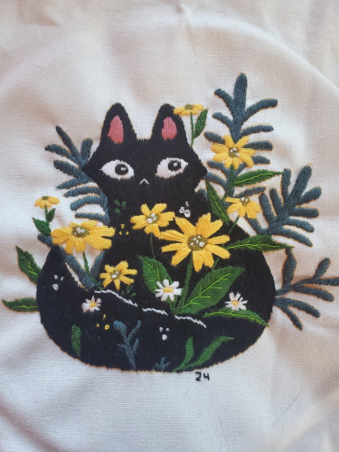 Embroidery design of a black cat surrounded by flowers and leaves