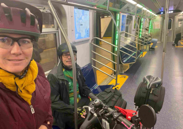 Two tired looking people equipped with bike kit sit in a mostly empty A train subway in nyc. 