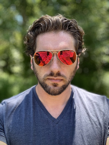 Selfie of me; brown hair with a short beard wearing a gray shirt and red aviator sunglasses which are crooked because one ear is higher than the other. 