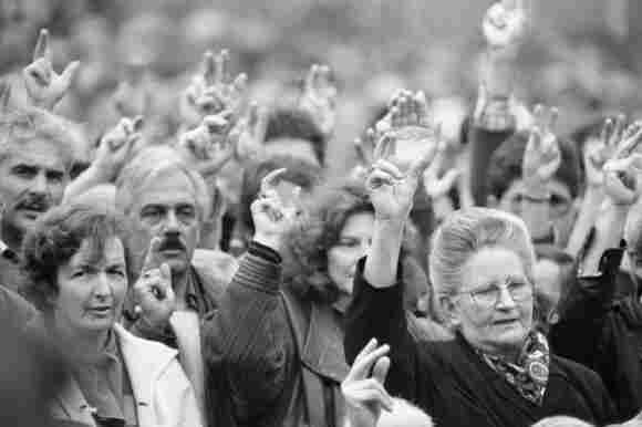 A B&W photo of a mixed group of men and women voting with their arms up on the town square of Appenzell Innerrhoden in 1991.