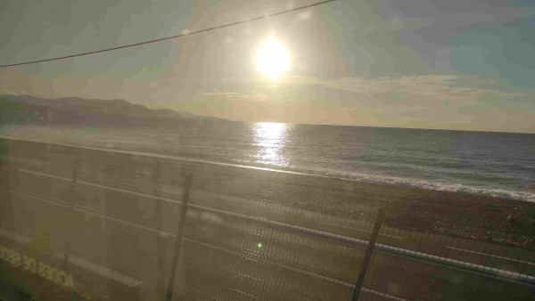 Vue sur la plage et la mer depuis le train. On voit le soleil levant au milieu de la photo.