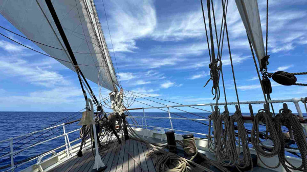 Bow of a sailing ship with a bell and pin rails. The tack of the fore course is almost on the deck. 