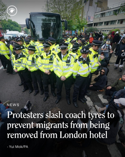 Protesters sitting on the ground in front of a State goons (Police), both of whom are in front of a vehicle State brought to kidnap migrants from London.

The caption says:

Protesters slash coach tyres to prevent migrants from being removed from London hotel.