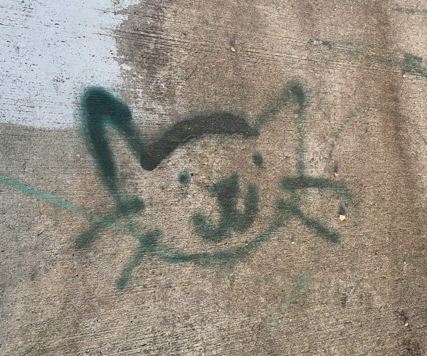A happy green spray painted cartoon kitty face on concrete.