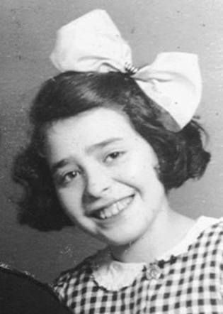 Black and white photograph of a young smiling girl. She is wearing a large bow in her hair and a checkered outfit.