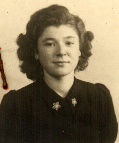 Vintage black-and-white photograph of a young girl with curly hair, wearing a dark blouse adorned with two floral pins.