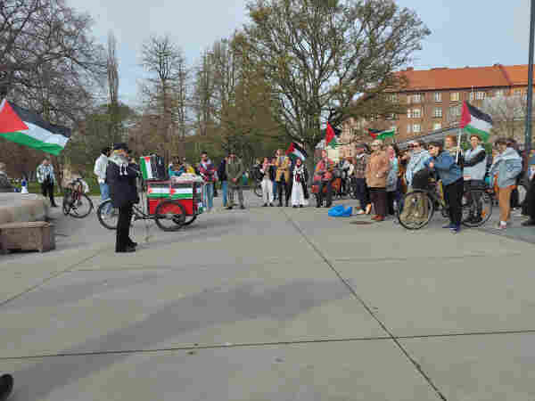Speech on Eurovision, EBU & Malmö's complicity in Israel's genocide. A cargo bike adorned with Palestinian flags, a speaker, and a listening crowd, waving Palestinian flags.