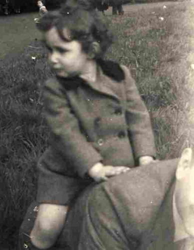 A young boy with curled hair is sitting on the back of a man whose face is not visible as it is cut by the frame of the photo.