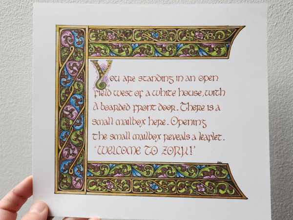 Calligraphied in brown ink insular script with a fancy bigger 'Y', "You are standing in an open filed west of a white house. There is a small mailbox here. Opening the small mailbox reveals a leaflet.
'Welcome to Zork!' "

It's framed on the left, top, and bottom with borders of Celtic knotwork and swirling leaves, in brown, blue, green, and purple, with gold lines and gold highlights.