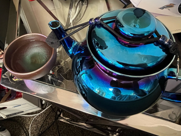 Blue and purple vibrant  iridescent glass tea pot and a  Japanese handle-free tea cup in paler iridescent purple and blue. 