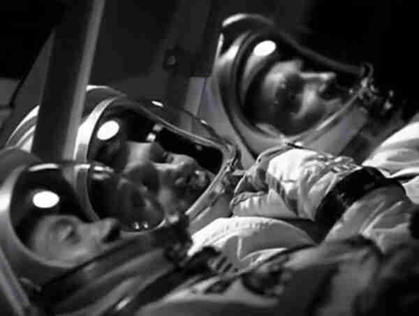 Three men in astronaut suits, lying on their backs in a test capsule