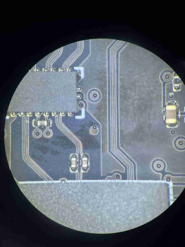 photo through microscope of components (chips, capacitors) and traces of a black pcb. there's a via in the middle of the photo whose drill hole is not where it belongs.