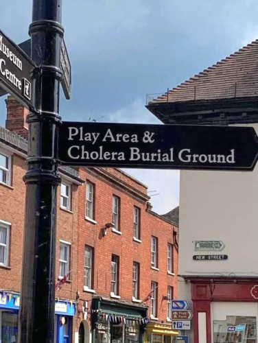 Street sign in an English town. Reads: play area & cholera burial ground