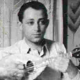 A man playing an instrument that resembles a ukulele or mandolin. He has short hair and is dressed in a shirt. 