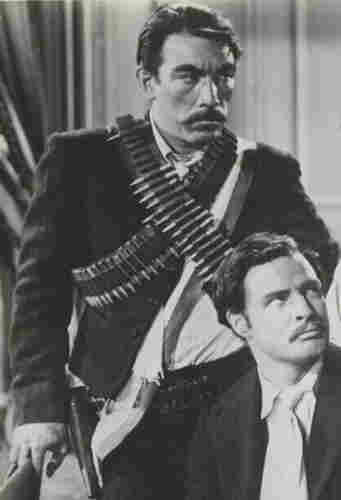 Anthony Quinn, as Eufemio Zapata (standing), with Marlon Brando as Emiliano Zapata in Viva Zapata! (1952). By Unknown author - eBay, Public Domain, https://commons.wikimedia.org/w/index.php?curid=128471494
