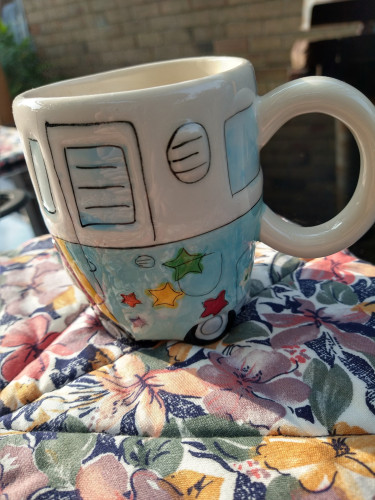Mug of tea on a garden table it is shaped like a VW Campervan with window, the bottom half is blue with bright stars 
