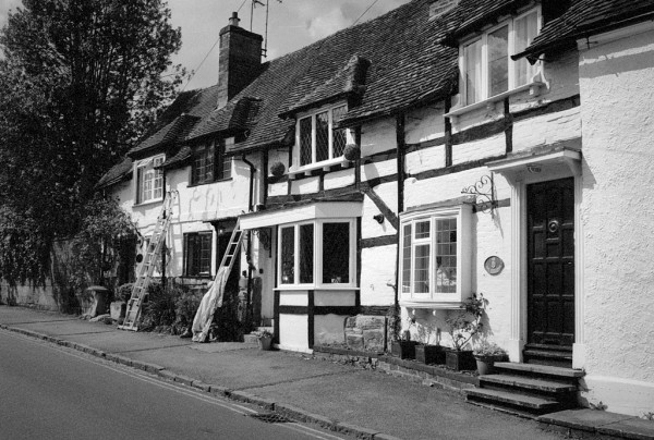 Black and white photo of a row of black and white cottages, with two decorator's ladders leaning against the third one.