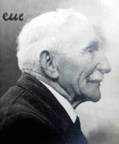 Profile portrait photograph of an older man. He has short grey hair and a grey moustache. His right profile is visible. He is dressed in a dark jacket and white shirt with tie. 