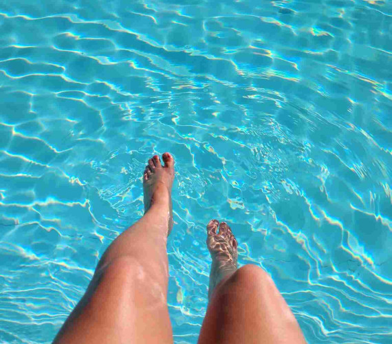 Feet dipped into a swimming pool with bright blue water