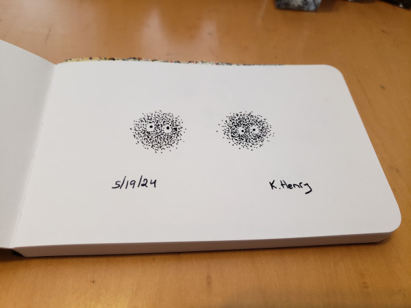 Hand drawn generative art in ink on an open page of my sketchbook. The pattern has two abstract faces made of little dots.