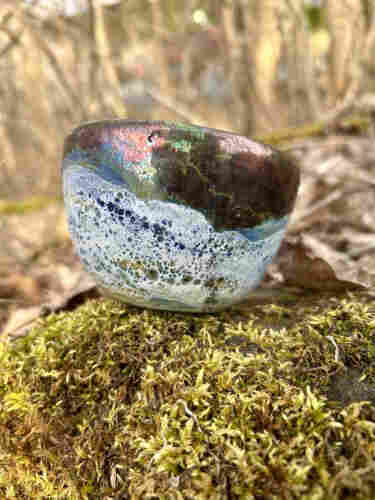 A raku fired tea bowl, the top is a coopery iridescent colour and the bottom is, mostly white with some blue.