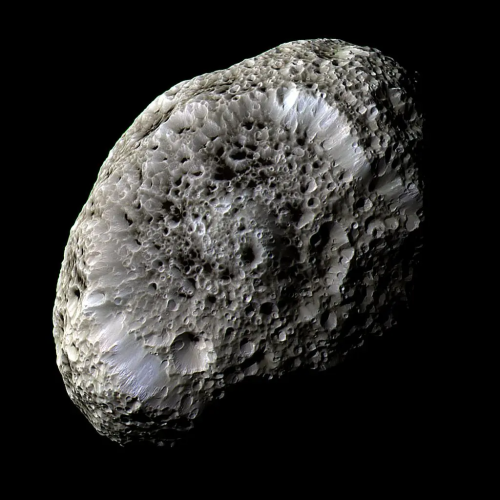 Saturn's moon Hyperion in a false-color view. It is a somewhat elongated irregular object with light and dark mottling and a pitted, almost waxy appearance, with craters at odd ground slopes that give them irregular non-circular shapes
