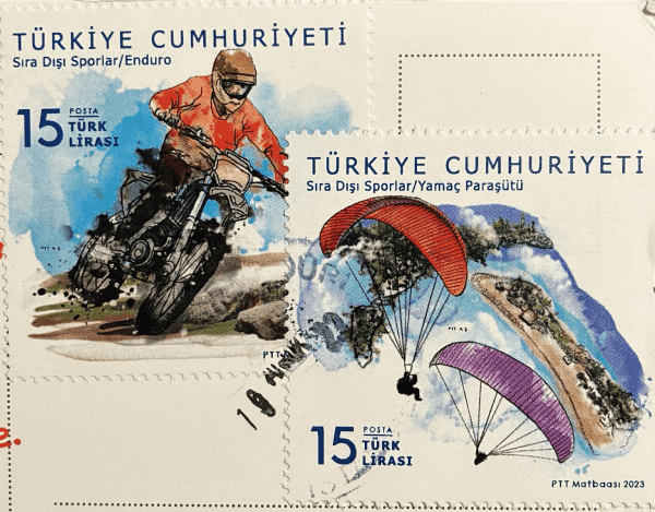 Two stamps from Turkey: top left stamp, shows a person riding a motorbike, and the bottom right stamp shows two people with colorful parachutes. 