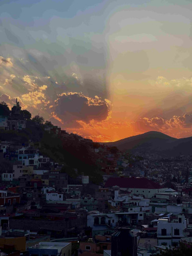 Orange sunset with far clouds casting shadows on the sky. In the foreground the hills of Guanajuato with the houses rising to the peaks.

Vertical view.