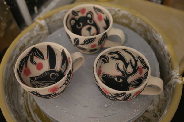 Interior of three handmade, unfired cappuccino cups. They are decorated with a bear, bunny and deer