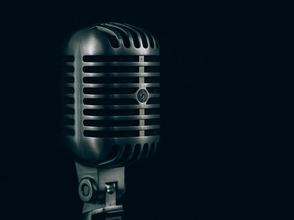 "A close-up of a condenser microphone in a steel casing against a black background"