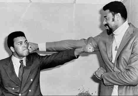 Promotional phot of Wilt Chamberlain and Muhammad Ali boxing, with the arms outstretched, showing Chamberlain’s advantage.
