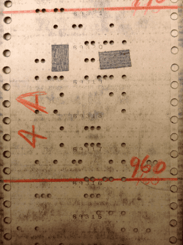 A photo of a punch card used in data processing and programming of early computers. The punch card has some of its hole covered with a tape.