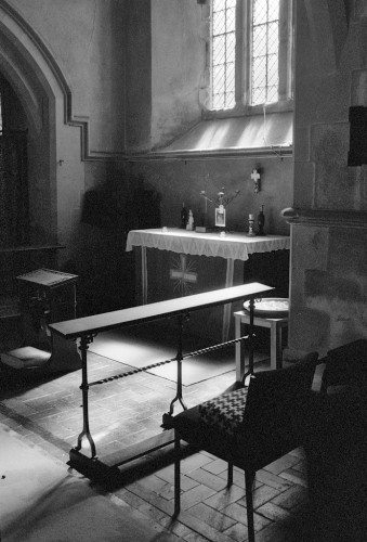 Portrait format black and white photo of light coming in through a plain church window into a small chapel.