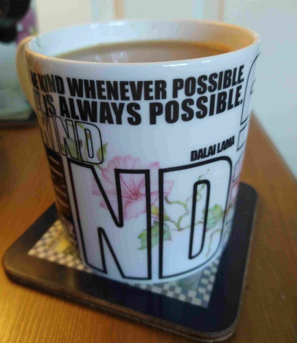 Mug of tea on a bedside cabinet, with a pink flower background, at the top in black lettering 'be kind whenever possible, it's always possible' 