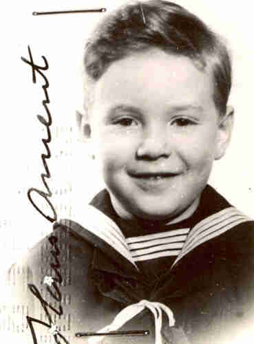 Black and white portrait photograph of a boy in sailor's garb. He has blonde hair, longer at the top, very short at the sides. He is smiling.