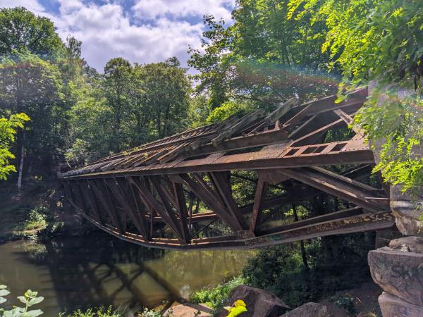 Metalowe przęsło uszkodzonego mostu widzi krzywo nad rzeką.