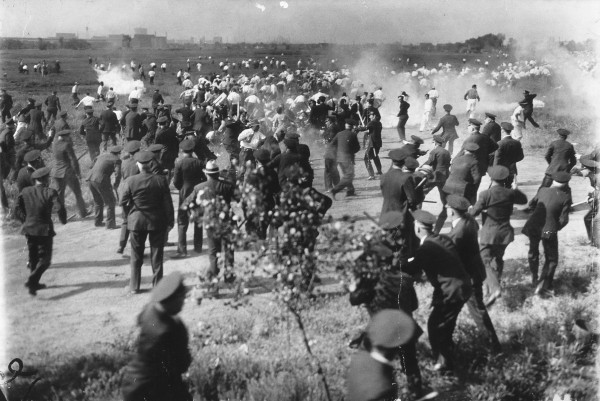 The Chicago Memorial Day Incident, photograph from the papers of the La Follette Committee: Police chasing workers through a field, guns drawn, with several billows of smoke in various locations in the field. By Unknown author or not provided - U.S. National Archives and Records Administration, Public Domain, https://commons.wikimedia.org/w/index.php?curid=19551258
