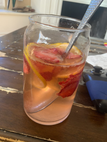 A jar of homemade lemonade with lemon and strawberry slices floating inside.