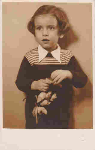 A portrait photo of a young boy. He is wearing a sweater with some stripes at the top. He is holding some toy in his hands - it looks like a fox or bunny. He has long hair reaching to his ears.