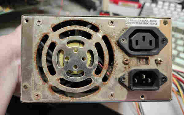 The back of an AT PSU: the fan opening is surrounded by rust, as are the the power connectors and the 115V/240V switch