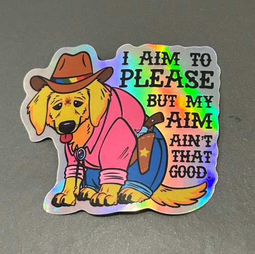 Holohraphic sticker of a yellow golden retriever puppy dressed as a cowboy. It says "I aim to please but my aim ain't that good" 