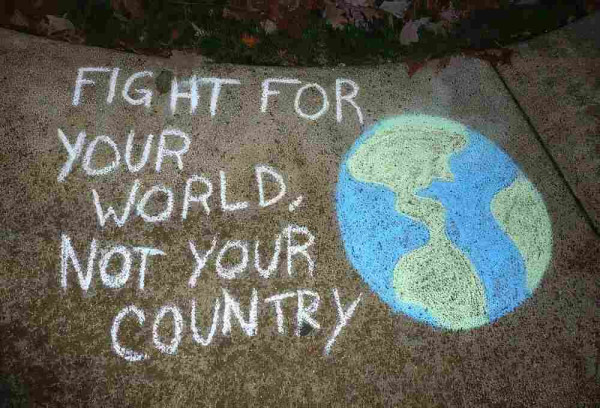 Street graffiti in chalk on a sidewalk. A blue and green drawing of Earth, along with this slogan: "Fight for your world, not your country."
