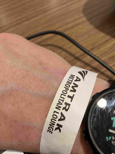 Photo of a wrist of a white person with a white paper wristband on it that reads “Amtrak metropolitan lounge”