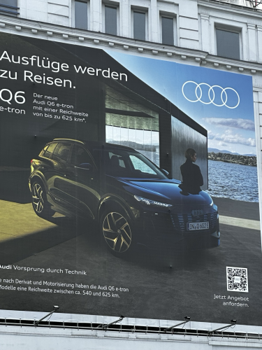 An einem Haus hängt eine riesigen Anzeige für einen riesigen E SUV von Audi.